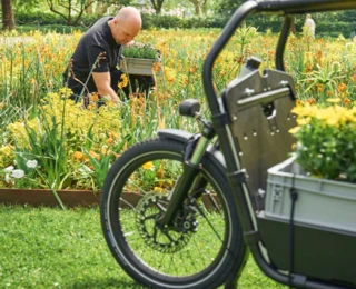 Ein mit Blumenkästen beladenes FS Vario ragt in das Bild. Im Hintergrund ist ein Gärtner bei der Arbeit zu sehen.