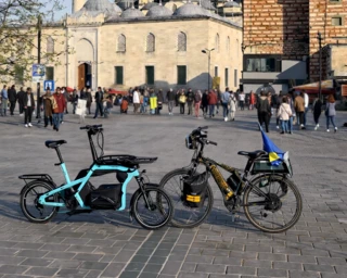 Ca Go CS und herkömliches Pedelec gegenübergestellt mit einer Menschenmenge und einer Moschee im Hintergrund