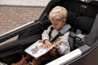 Ein kleines Kind sitzt mit einem 5-Punkt-Gurt angeschnallt in einem Ca Go FS Life und ließt ein Bilderbuch.