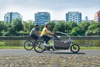 Mann und Frau fahren mit Fahrrädern über einen Weg. Die Frau fährt ein FS Life, in der Box sitzt ein Kind.