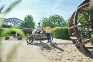 Mann und Frau sind mit FS200 Life Family-Plus auf einem Spielplatz. In der Box sitzt ein Kind.