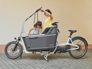 Ein Mädchen steigt in die Transportbox des FS200 Life Family Box. Die Mutter hält das All-Weather-Top auf.