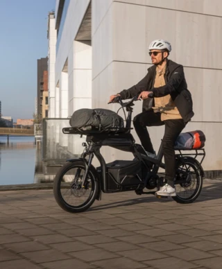 Ein Mann fährt mit dem Ca Go CS an einem Fluss entlang- Das Fahrrad ist mit einigen Gepäckträgern und Taschen ausgestattet.