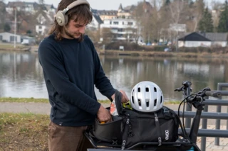 Mann nimmt etwas aus der Fahrradtasche auf dem Front Rack des Ca Go CS heraus und trägt Kopfhörer