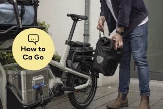 Mann befestigt Packtasche am Ca Go CS. Daneben steht "How to Ca Go" auf gelbem Untergrund