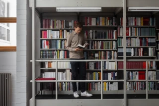 Lennart Schäfer von der Literadtour steht in einer Bibliothek und liest in einem Buch