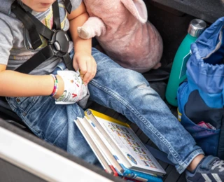 Ein kleines Kind sitzt mit einem 5-Punkt-Gurt angeschnallt in einer mit Spielzeug gefüllten EPP-Box.